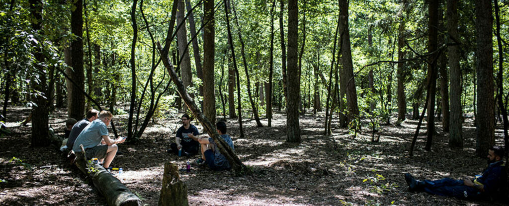 Een groepje deelnemers zit in het bos met elkaar te praten.